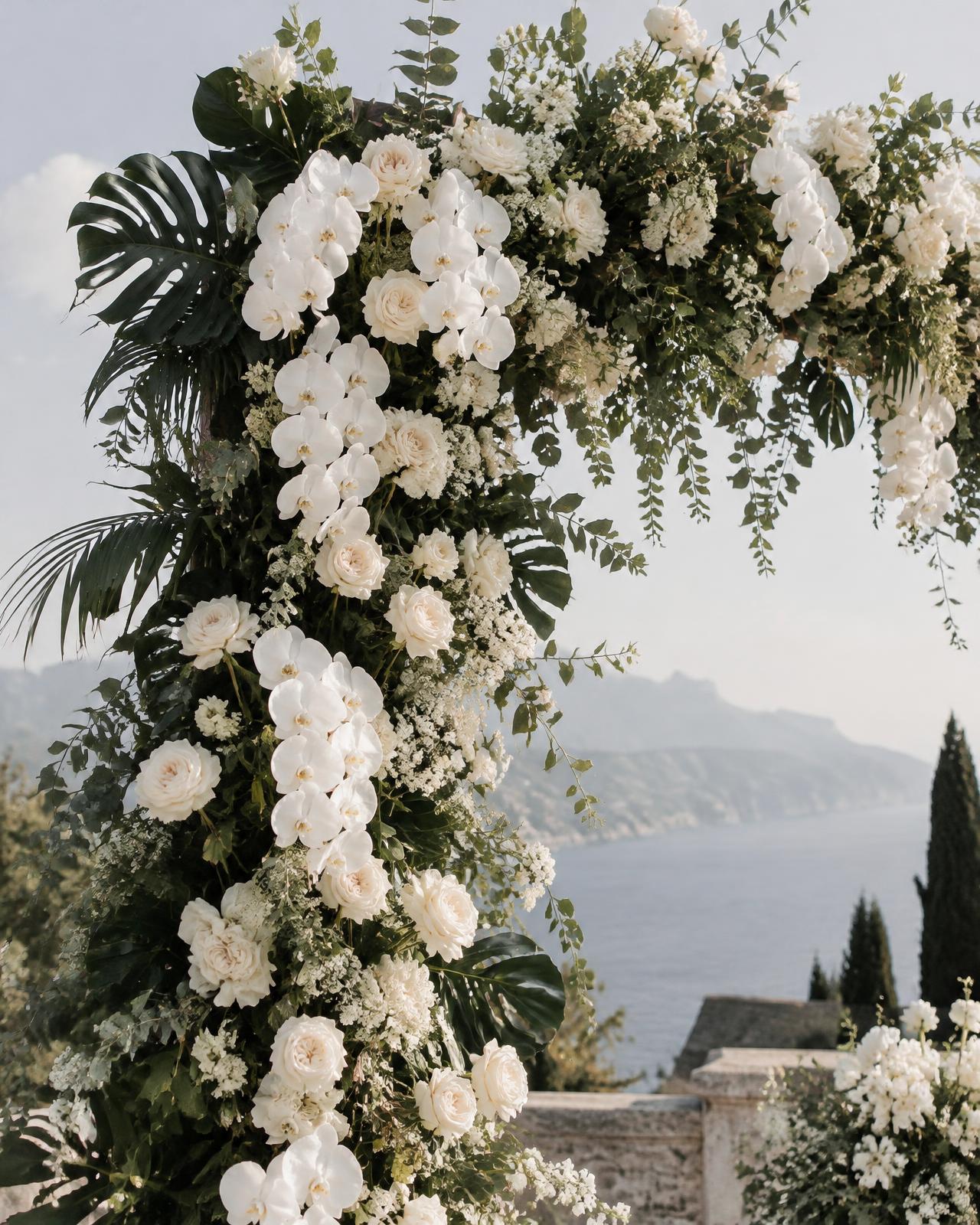 A floral arch of white orchids, garden roses and tropical leaves above the sea